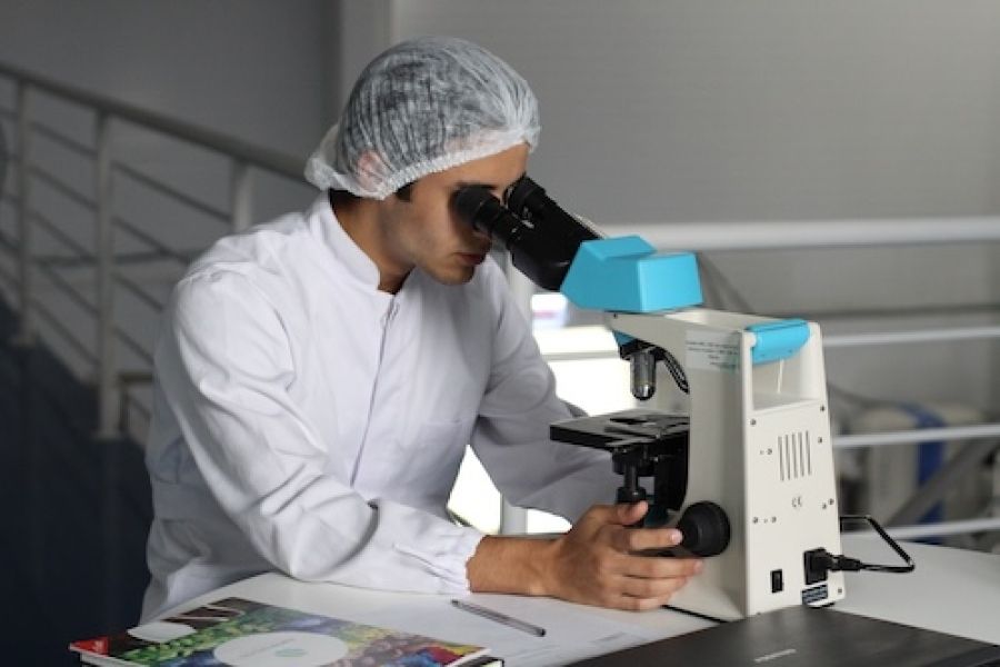 Person in a hat looking through a microscope.