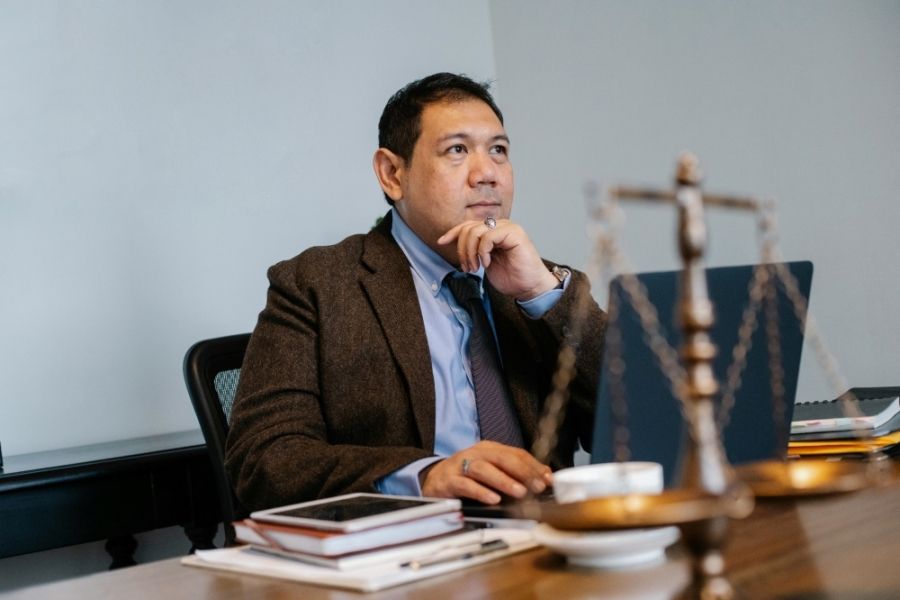 man sitting around a wooden table looking off into the distance. Their is a justice weight scale in the foreground.