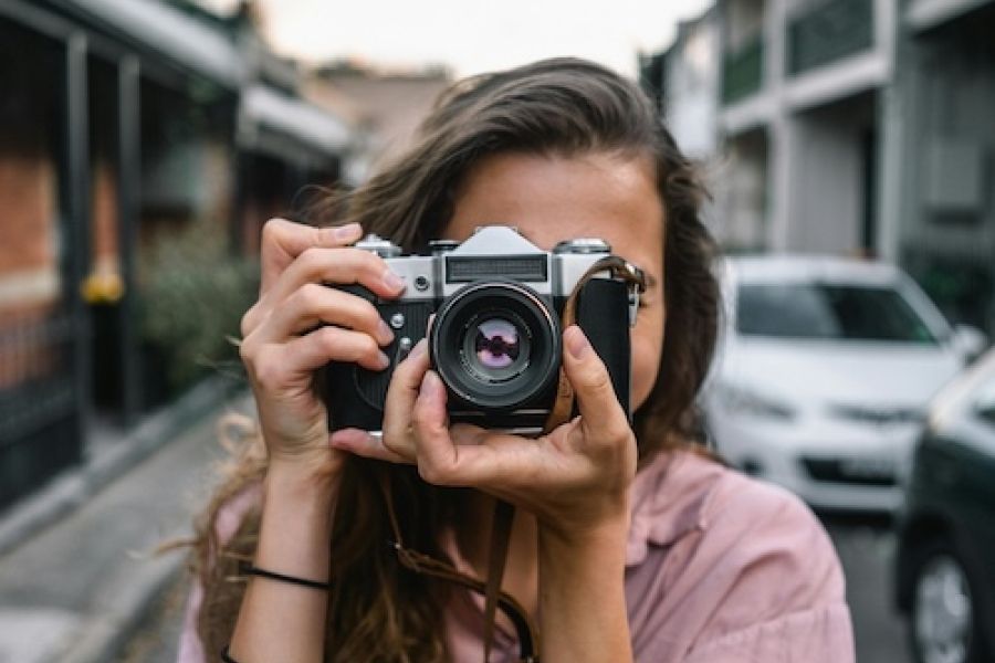 Woman with a camera pointing it at the camera as if it's looking at you.
