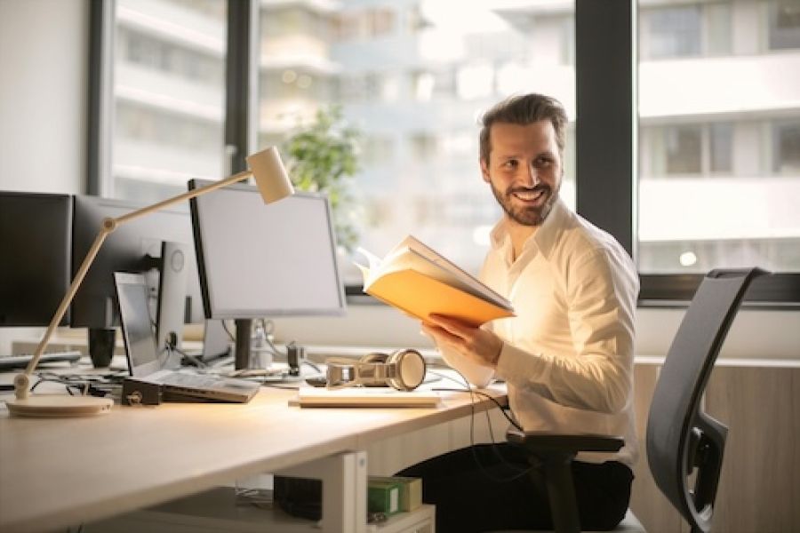 Man at a computer who is also looking at a book and smiling.