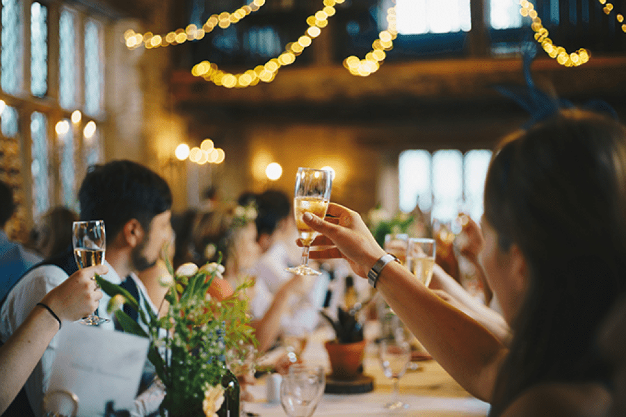 Photo of a room decorated for a wedding. Several people are raising their glasses.